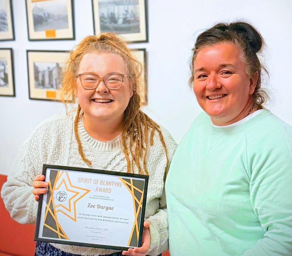 Zoe Dargue holding her Spirit of Blantyre certificate beside another attendee