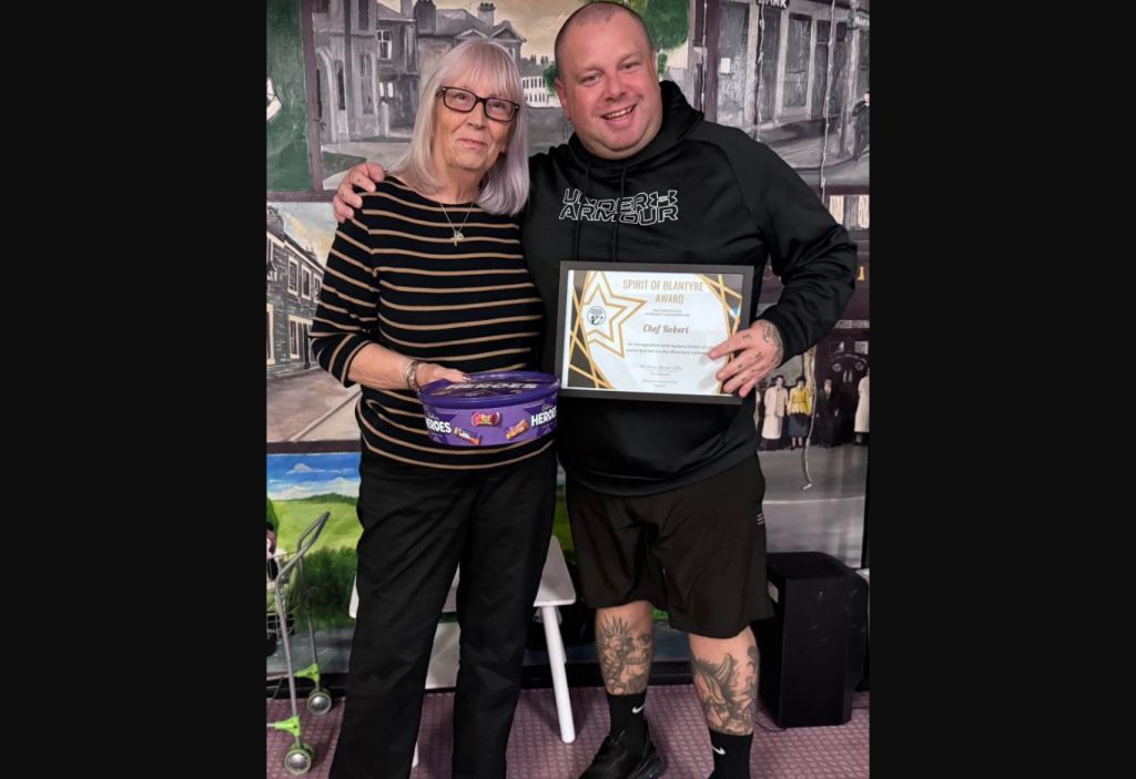 Chef Robert holding his Spirit of Blantyre Award beside a Community Council representative